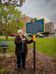 Little Falls Historical Society Board Member and City Historian, Pat Stock, after cleaning the Herkimer County Bank historic marker.